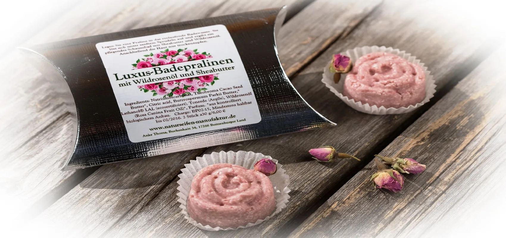 Luxus-Badepralinen mit Wildrosenöl und Sheabutter, präsentiert in einer eleganten Verpackung auf einem Holztisch, dekoriert mit getrockneten Rosenknospen.